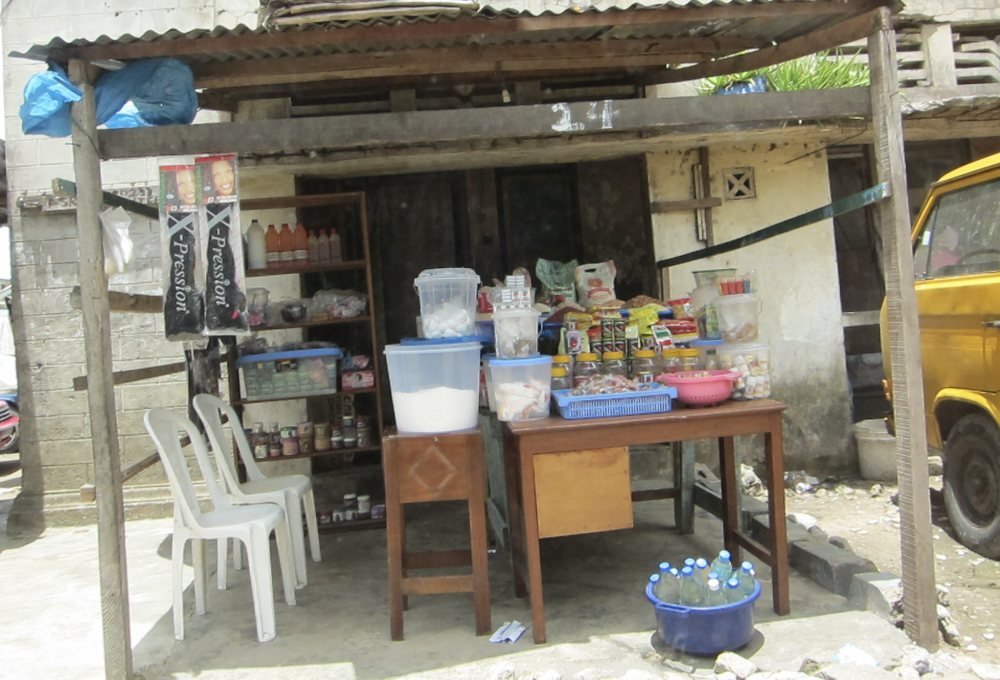 A small roadside shop with goods on tables under a corrugated roof